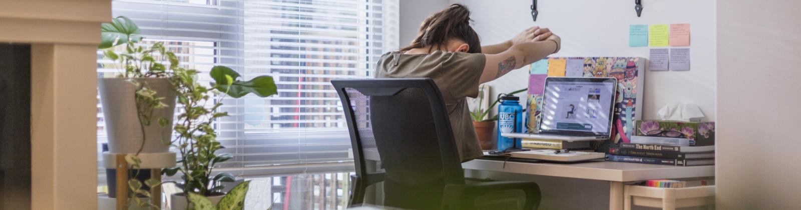 A student sitting at their work from home desk space while doing arm stretches