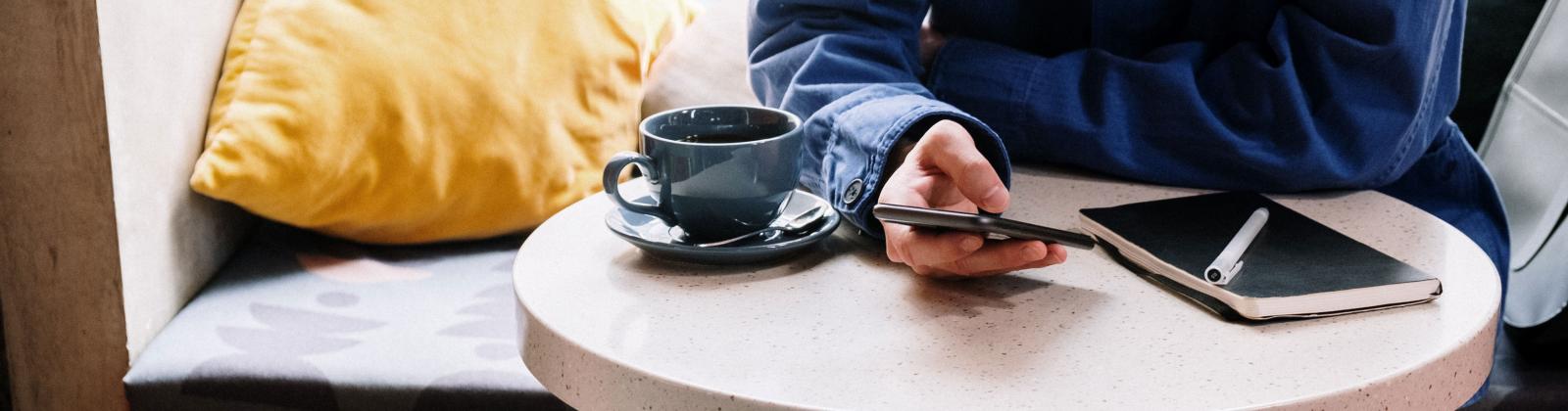 A student seated at a table in a cafe while on their phone